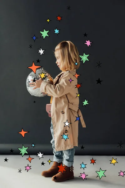 Side view of child in trench coat holding disco ball on black background with stars illustration — Stock Photo