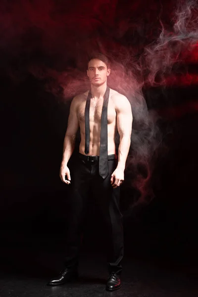 Full length view of sexy shirtless man standing in smoke on black — Stock Photo