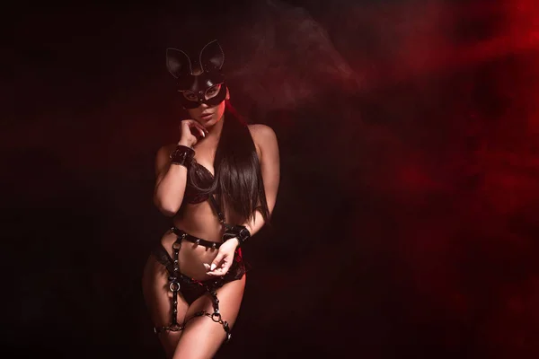 Sexy bdsm chica en lencería y máscara en rojo humo en negro - foto de stock
