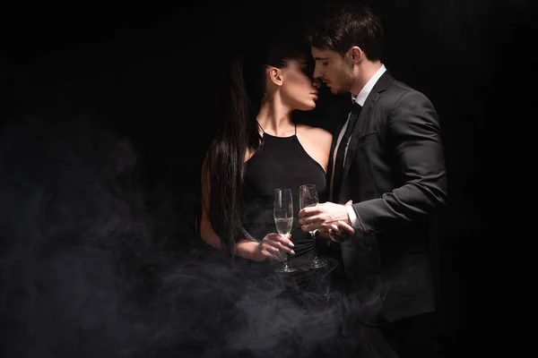 Pareja con estilo con copas de champán besos en negro - foto de stock