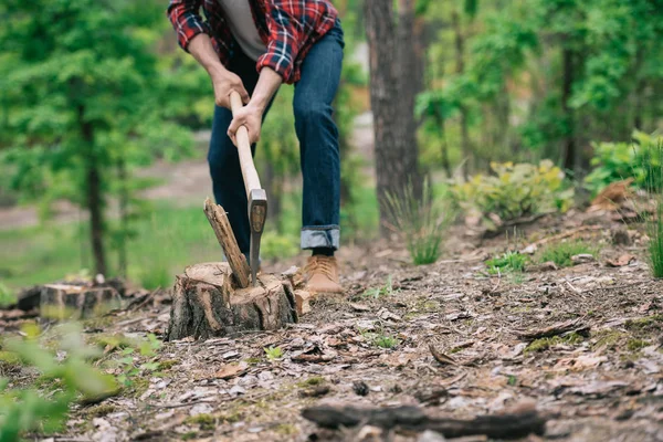 Vista parziale del taglialegna in jeans denim che taglia legna con ascia nella foresta — Foto stock