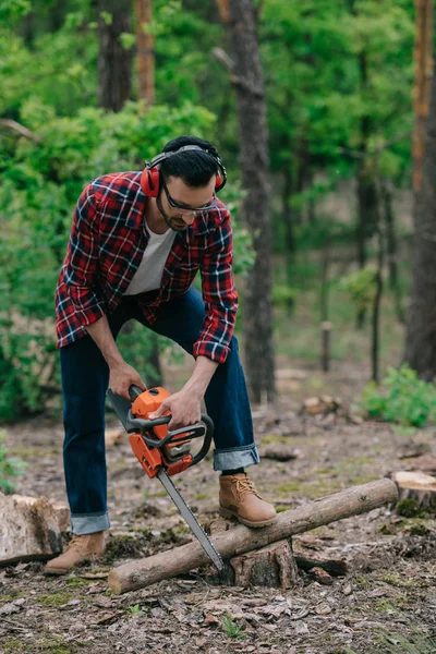 Holzfäller mit lärmintensiven Kopfhörern hackt mit Kettensäge Holz im Wald — Stockfoto