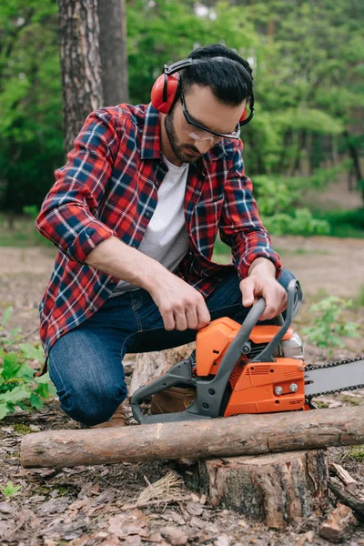 Waldarbeiter im karierten Hemd und Gehörschutz stellen Kettensäge im Wald ein — Stockfoto