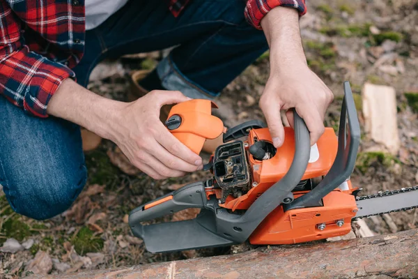 Cropped view of lumberer in plaid shirt fixing chainsaw in forest — Stock Photo