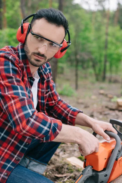 Boscaiolo serio con paraorecchie e protettori acustici che distolgono lo sguardo nella foresta — Foto stock