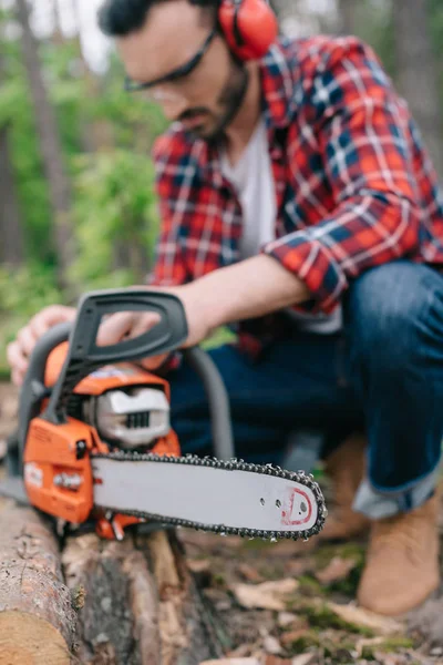 Selective focus of lumberjack repairing electric chainsaw in forest — Stock Photo