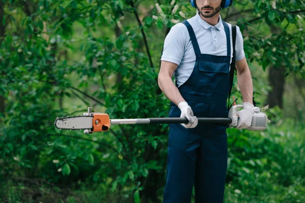 Abgeschnittene Ansicht des Gärtners in Overalls mit Teleskopstangensäge im Garten — Stockfoto