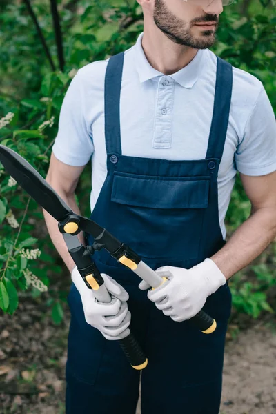 Обрезанный вид садовника в комбинезоне проведение триммер в саду — стоковое фото
