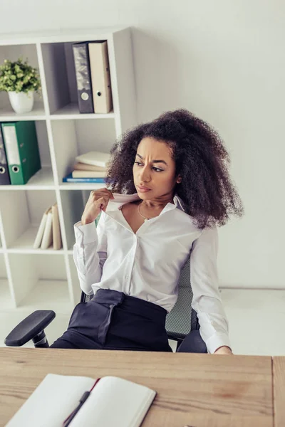 Attractive african american woman suffering from summer heat while sitting at workplace in office — Stock Photo