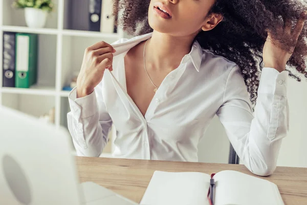 Vue partielle d'une femme d'affaires afro-américaine assise sur le lieu de travail et souffrant de chaleur — Photo de stock