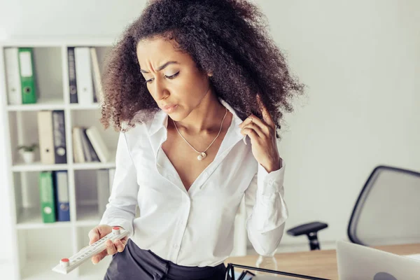 Dissatisfied african american businesswoman looking at thermometer in office — Stock Photo