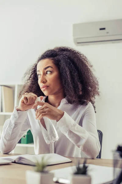 Enfoque selectivo de la mujer de negocios ameriacn africana insatisfecha mirando hacia otro lado mientras sostiene la botella de plástico con agua - foto de stock