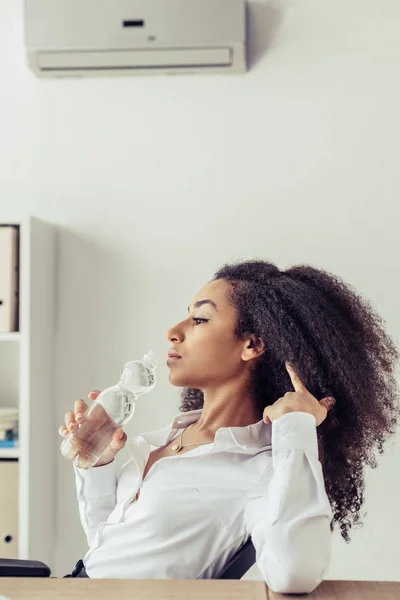 Attractive african american businesswoman drinking water while suffering from heat in office — Stock Photo