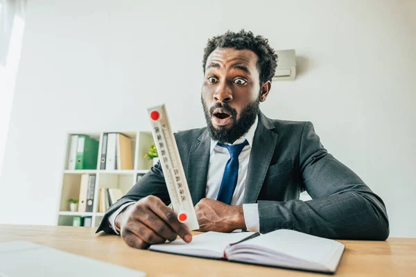 Chocado empresário afro-americano olhando para o termômetro enquanto sofre de calor no escritório — Fotografia de Stock