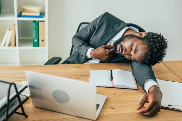 Agotado hombre de negocios afroamericano acostado en el escritorio mientras sufría de calor de verano en la oficina - foto de stock