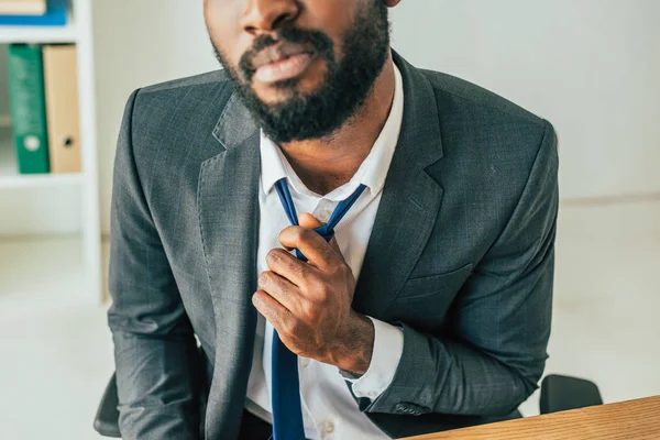 Visão parcial do empresário afro-americano tocando gravata enquanto sofre de calor no escritório — Fotografia de Stock