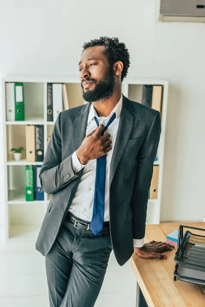 Erschöpfter afrikanisch-amerikanischer Geschäftsmann steht in der Nähe seines Arbeitsplatzes und leidet unter Hitze im Büro — Stockfoto