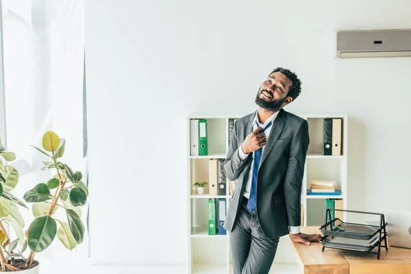 Handsome afrcian american businessman standing near workplace and looking up while suffering from summer heat — Stock Photo
