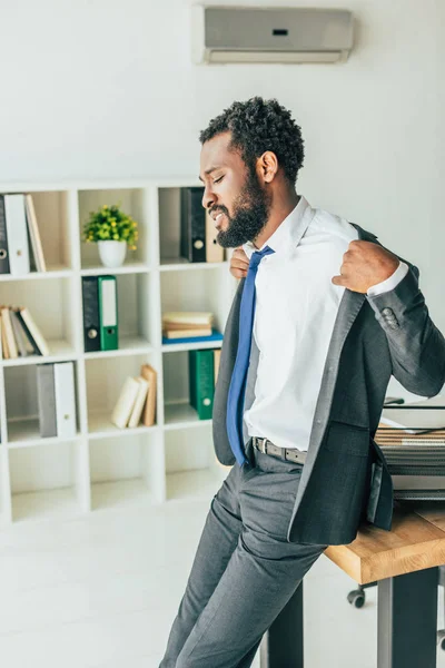 Exhausted african american businessman undressing while suffering from heat in office — Stock Photo