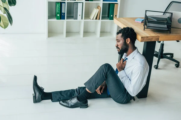 Exhausted african american businessman sitting on floor while suffering from summer heat — Stock Photo