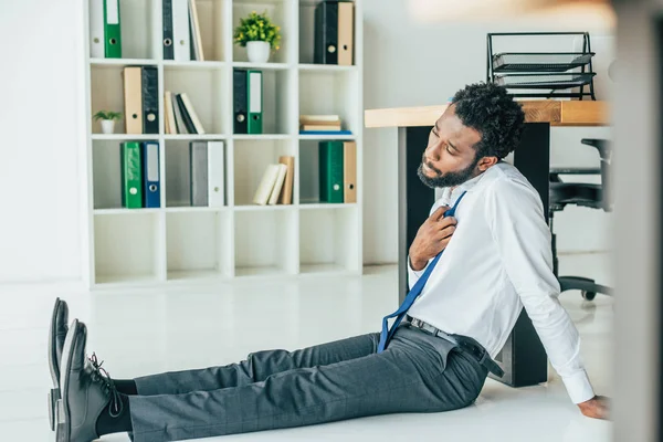 Enfoque selectivo del joven hombre de negocios afroamericano sentado en el suelo mientras sufre de calor de verano - foto de stock