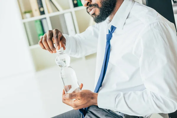 Vue partielle d'un homme d'affaires afro-américain ouvrant une bouteille en plastique avec de l'eau tout en souffrant de chaleur — Photo de stock
