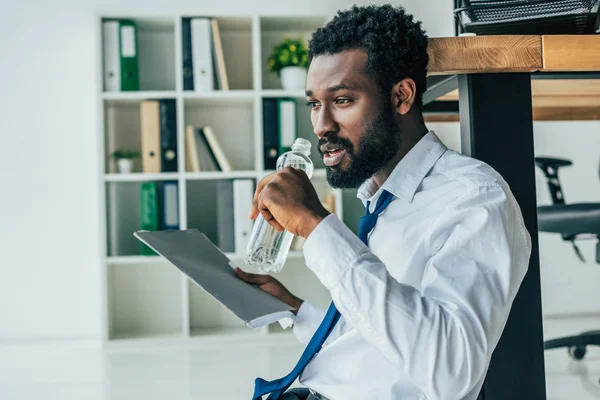 Épuisé homme d'affaires afro-américain boire de l'eau tout en souffrant de chaleur — Photo de stock