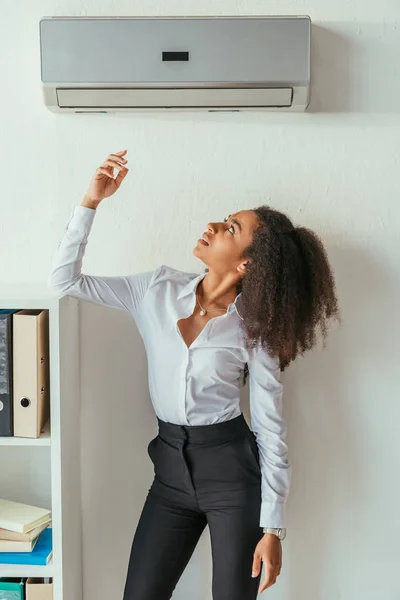 Atractiva mujer de negocios afroamericana de pie bajo aire acondicionado en la oficina - foto de stock