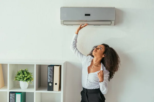 Jolie femme d'affaires afro-américaine touchant climatiseur tout en souffrant de chaleur au bureau — Photo de stock