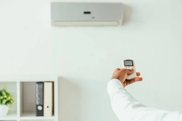 Vue recadrée de l'homme d'affaires afro-américain tenant climatiseur télécommande dans le bureau — Photo de stock