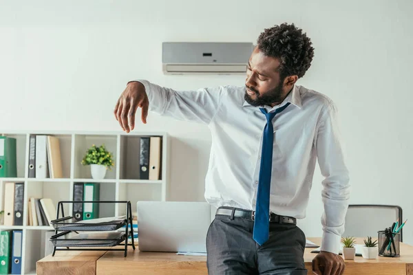 Dissatisfied african american businessman looking at sweaty shirt while suffering from summer heat — Stock Photo