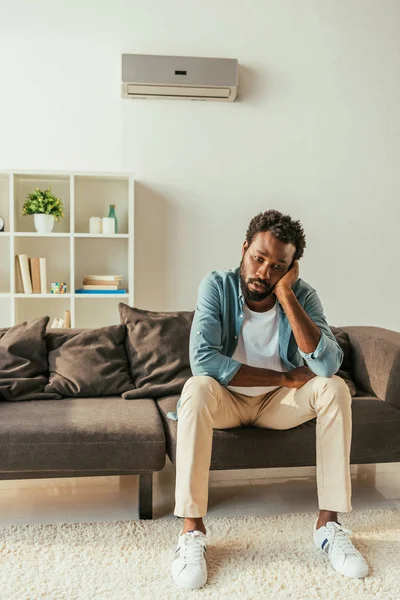 Erschöpfter afrikanisch-amerikanischer Mann leidet unter Sommerhitze, während er zu Hause auf Sofa sitzt — Stockfoto