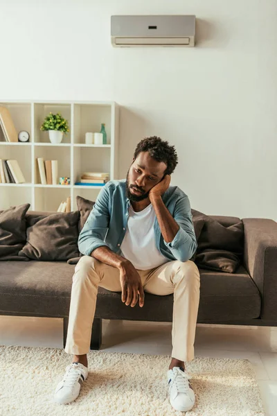 Exausto empresário afro-americano sentado no sofá e sofrendo de calor de verão — Fotografia de Stock