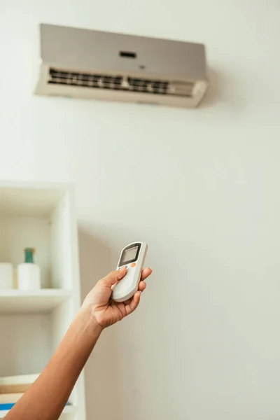 Partial view of african american woman using air conditioner remote controller — Stock Photo