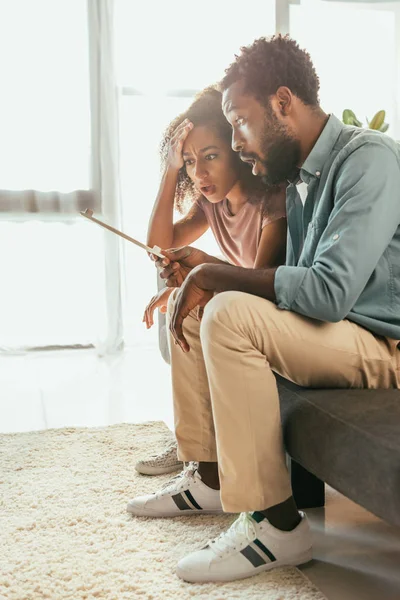 Sorprendido afroamericano hombre y mujer mirando termómetro mientras sufría de calor de verano en casa - foto de stock