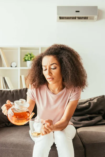 Виснажена афроамериканська жінка вливає чай в чашку, страждаючи від літньої спеки вдома — стокове фото