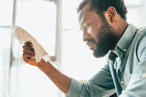 Dissatisfied african american man holding napkin while suffering from summer heat at home — Stock Photo