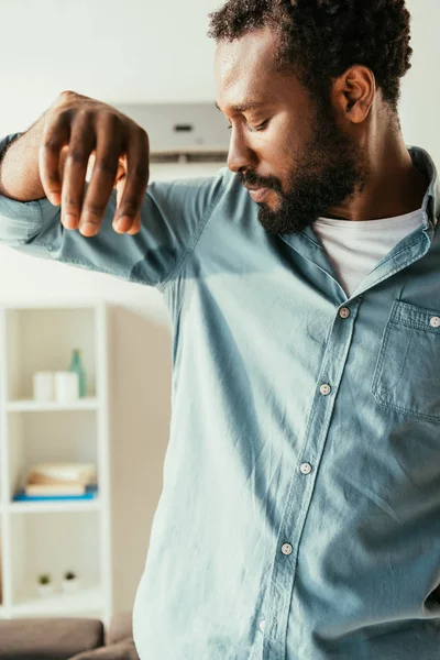 Joven afroamericano hombre en sudorosa camisa sufriendo de aummer calor en casa - foto de stock