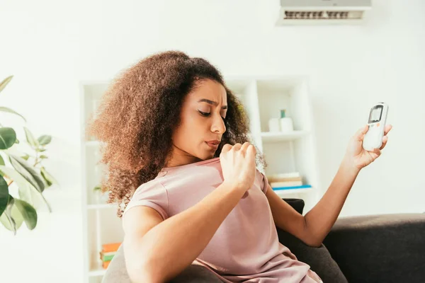 Jovem mulher afro-americana em camisa suada segurando controlador remoto ar condicionado — Fotografia de Stock