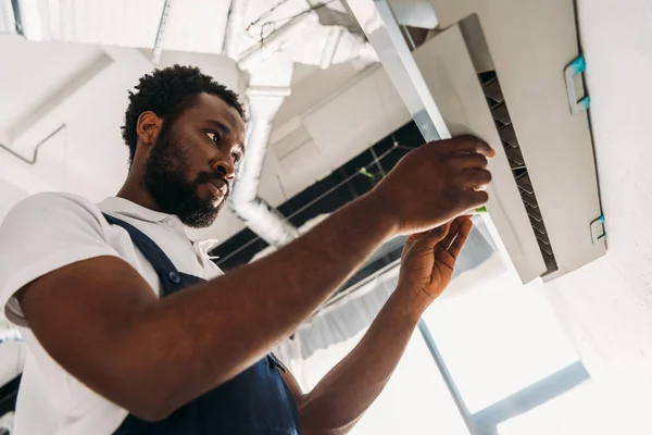Réparateur afro-américain concentré debout sur l'échelle et la fixation climatiseur — Photo de stock