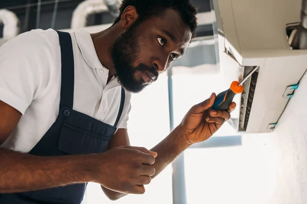 Réparateur afro-américain attentif fixant climatiseur avec tournevis — Photo de stock