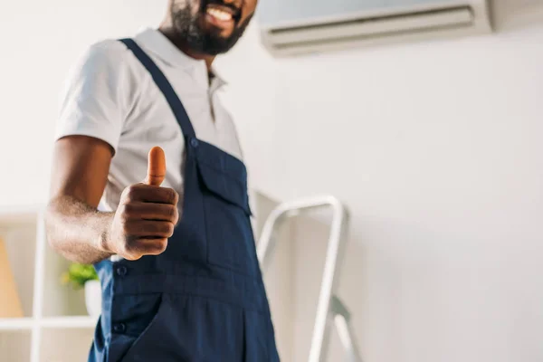 Partial view of smiling african american repairman showing thumb up at camera — Stock Photo