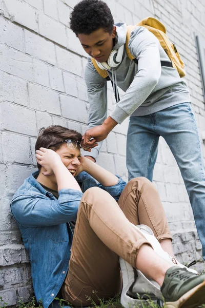 Agresivo y morena afroamericano chico quitándose gafas de asustado chico - foto de stock