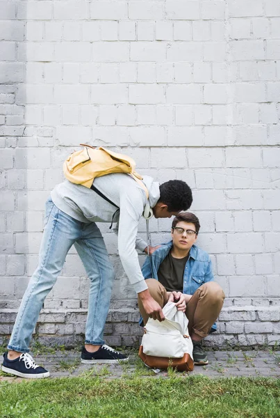Aggressive african american boy taking backpack from frightened boy in glasses — Stock Photo