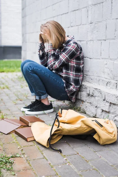 Aufgebracht und blonder Teenager in Hemd und Jeans sitzt an der Wand zwischen Büchern — Stockfoto