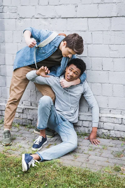 En colère garçon en chemise taureau, va frapper afro-américain effrayé garçon en sweat à capuche — Photo de stock