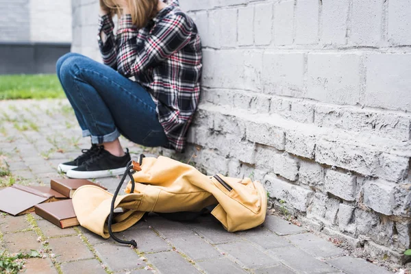 Adolescente desapontado e loiro em camisa e jeans sentado perto da parede entre os livros — Fotografia de Stock