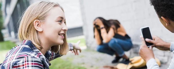 Plano panorámico de chico afroamericano y adolescente rubio señalando con el dedo y disparando adolescente asustado - foto de stock