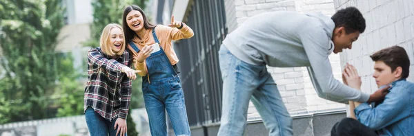 Panoramic shot of african american boy in hoodie and jeans bulling boy and teenager shooting it and pointing with fingers — Stock Photo