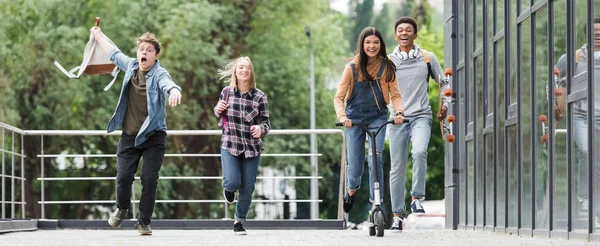 Panoramic shot of happy friends smiling, running and riding scooter — Stock Photo